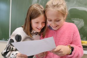 Dwie roześmiane dziewczynki skupione nad swoimi notatkami przy tablicy