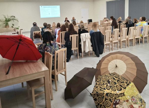 rozłożone parasolki a w tle ludzie słuchający prelekcji