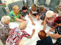 Seniorzy wokół stołu robiacy wspólnie prace plastyczna