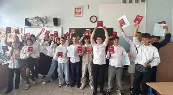 Duża grupa dzieci stoi z Paszportami Sportowymi w rękach