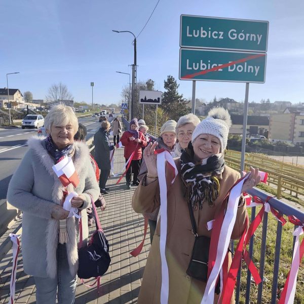 Seniorzy wieszają biało czerwone wstążki na moście