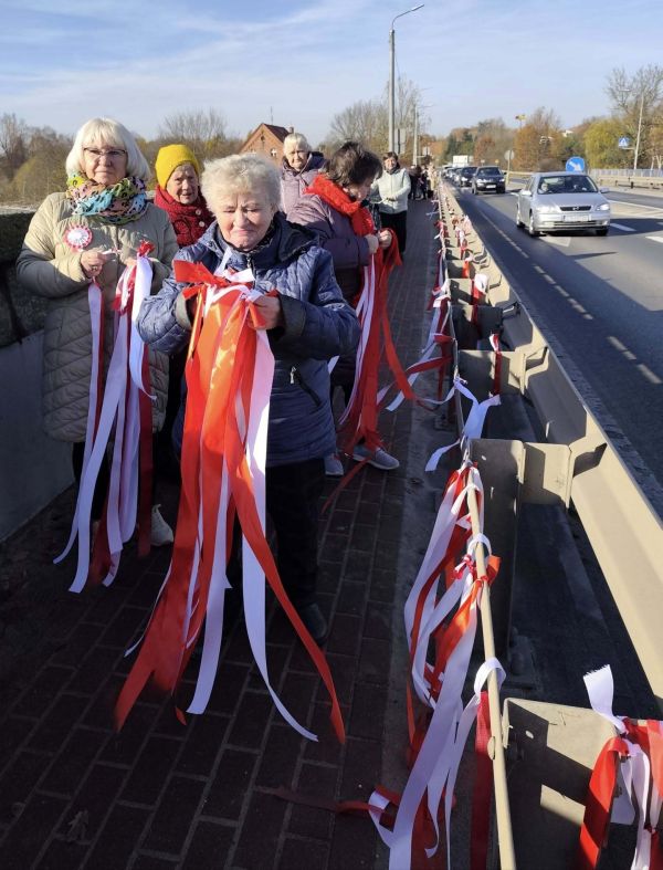 Seniorzy wieszają biało czerwone wstążki na moście