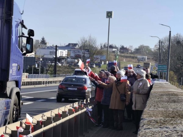 Seniorzy na moście machają flagami do samochodów