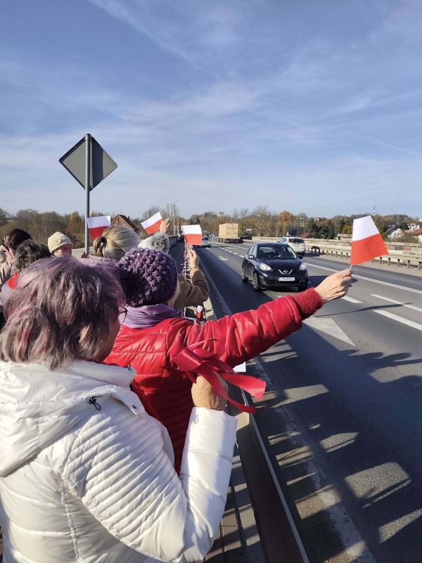 Seniorzy na moście machają flagami do samochodów